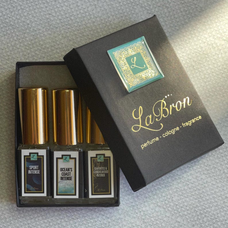 May include: A black box with gold lettering that reads "La Bron perfume - cologne - fragrance". The box contains three small glass bottles with gold caps and labels. The labels read "Sport Intense", "Ocean's Coast Intense", and "Oakmoss & Sandalwood Intense".