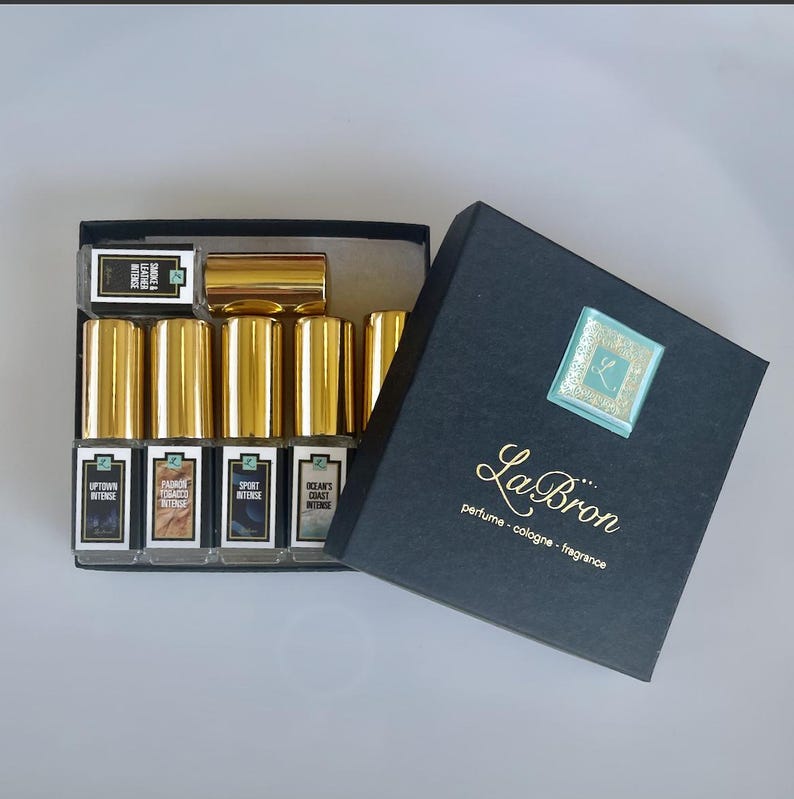 May include: A black box with gold lettering that reads "La Bron perfume-cologne-fragrance". The box contains eight small glass bottles with gold caps and labels that include the names "Uptown Intense", "Padron Tobacco Intense", "Sport Intense", and "Ocean's Coast Intense".