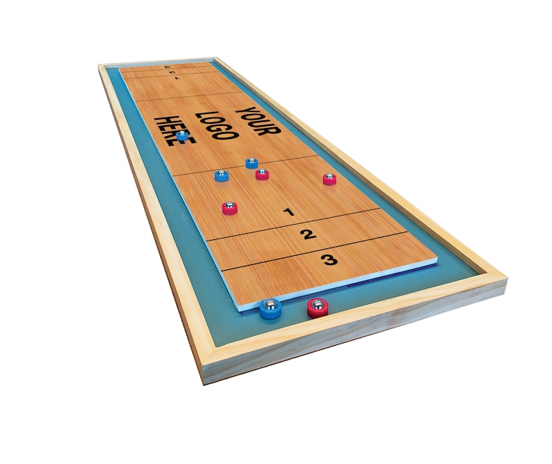 May include: A wooden shuffleboard game with blue and red playing pieces. The game has a wooden frame and a blue felt surface. The game has a wooden surface with the words "YOUR LOGO HERE" printed on it.