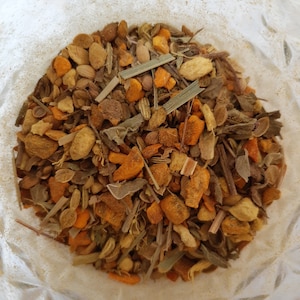 May include: A close-up of a mixture of dried herbs and spices, including turmeric, ginger, and lemongrass. The mixture is a vibrant orange and yellow color and is perfect for making tea or adding flavor to dishes.