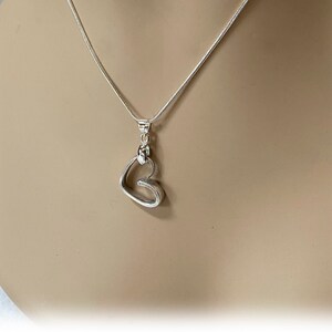 May include: A silver necklace with a heart-shaped pendant. The pendant is made of two interlocking hearts.