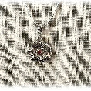 May include: A silver pendant necklace with a flower design and a small red gemstone in the center.
