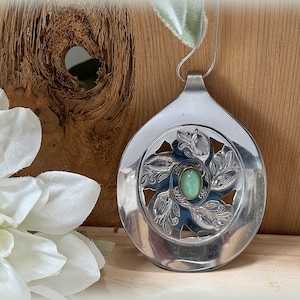 Può includere: Una collana con un ciondolo a forma di cucchiaio d'argento con una pietra preziosa verde incastonata al centro di un design decorativo tagliato.