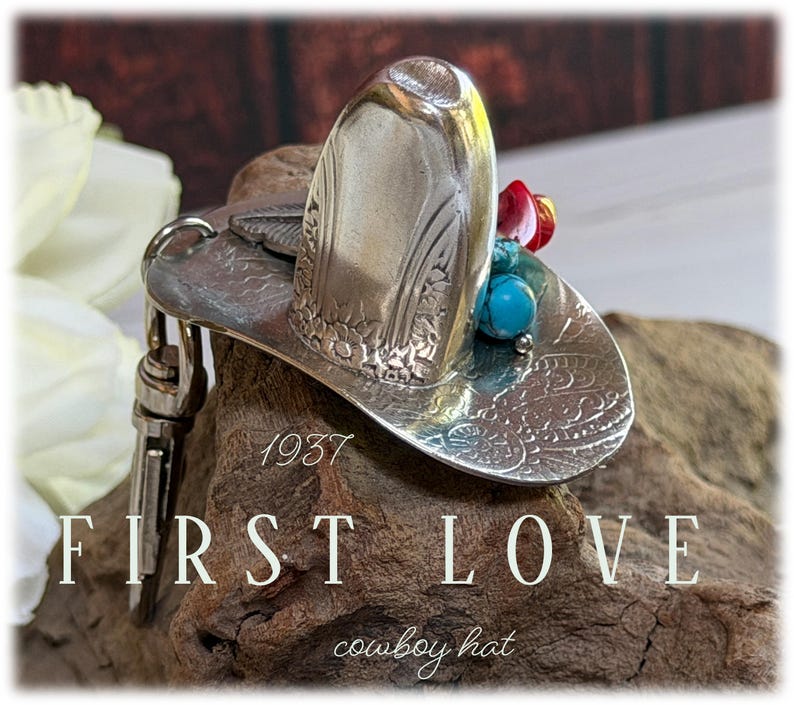 May include: A silver-toned metal keychain shaped like a cowboy hat with embossed floral patterns. The hat is adorned with small turquoise and red beads. The text 1937 FIRST LOVE cowboy hat is visible on the image, along with a metal lobster clasp.