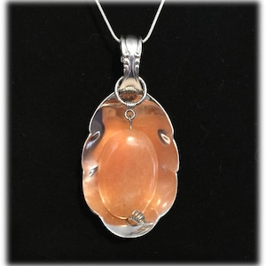 May include: A silver spoon pendant necklace with a peach-coloured stone set in the bowl of the spoon.