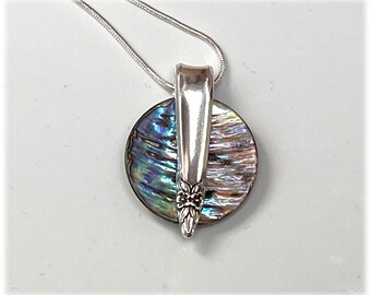 Pode incluir: Um colar de prata com um pingente feito de uma colher reutilizada e uma peça redonda de concha de abalone iridescente.