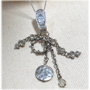 May include: A silver-toned pendant necklace featuring a spoon-shaped top with a crown and profile design. The necklace has a circular charm and dangling chains with clear crystal accents, creating a vintage aesthetic.