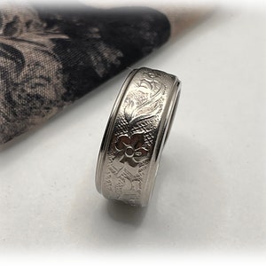Puede incluir: Un anillo de banda de plata con un diseño floral grabado alrededor de la banda.