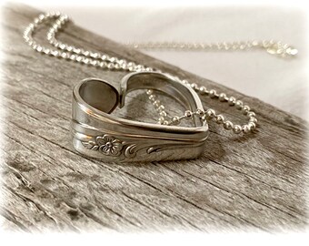 May include: A silver heart-shaped pendant necklace made from a repurposed spoon. The pendant features a floral design and is attached to a silver chain.