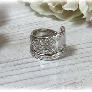 Puede incluir: Un anillo de plata hecho de una cuchara vintage con un diseño floral. El anillo está hecho de dos piezas de cuchara que se unen.