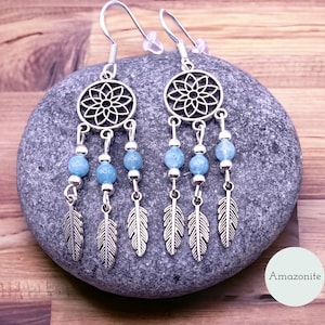 Może przedstawiać: Srebrne kolczyki w kształcie łapacza snów z niebieskimi koralikami z amazonitu i zawieszkami w kształcie piór.
