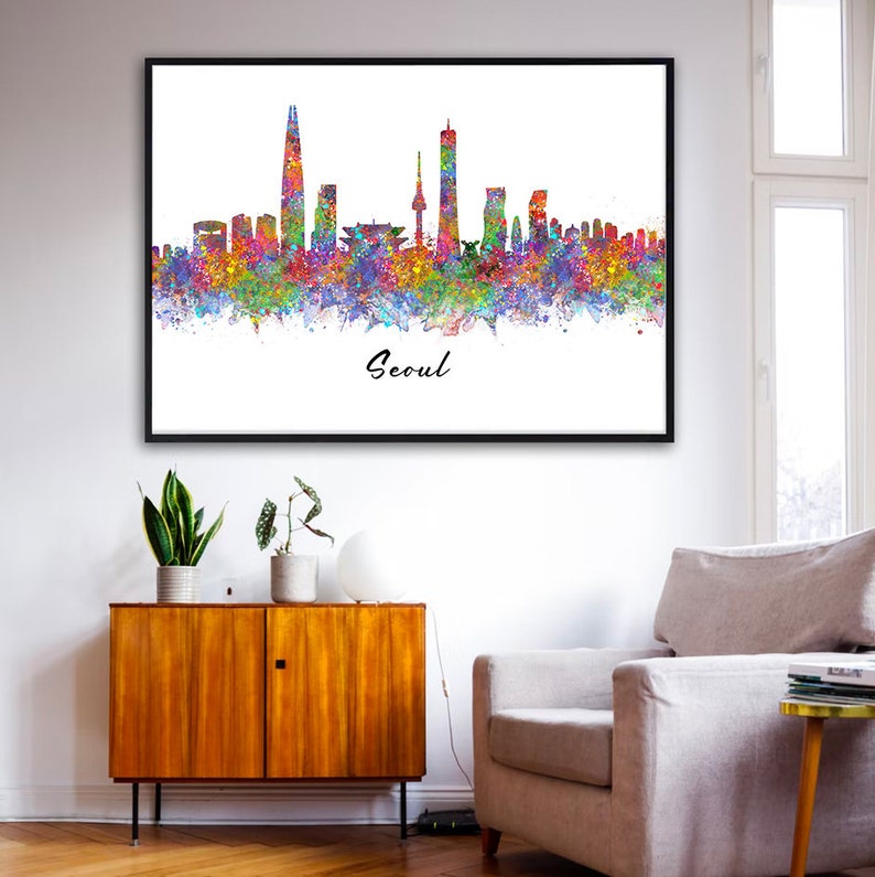 May include: A watercolor painting of the Seoul skyline with colorful splashes of paint. The city's iconic skyscrapers are visible, including the Lotte World Tower and the N Seoul Tower. The painting is framed in black and the word "Seoul" is written in black script at the bottom.
