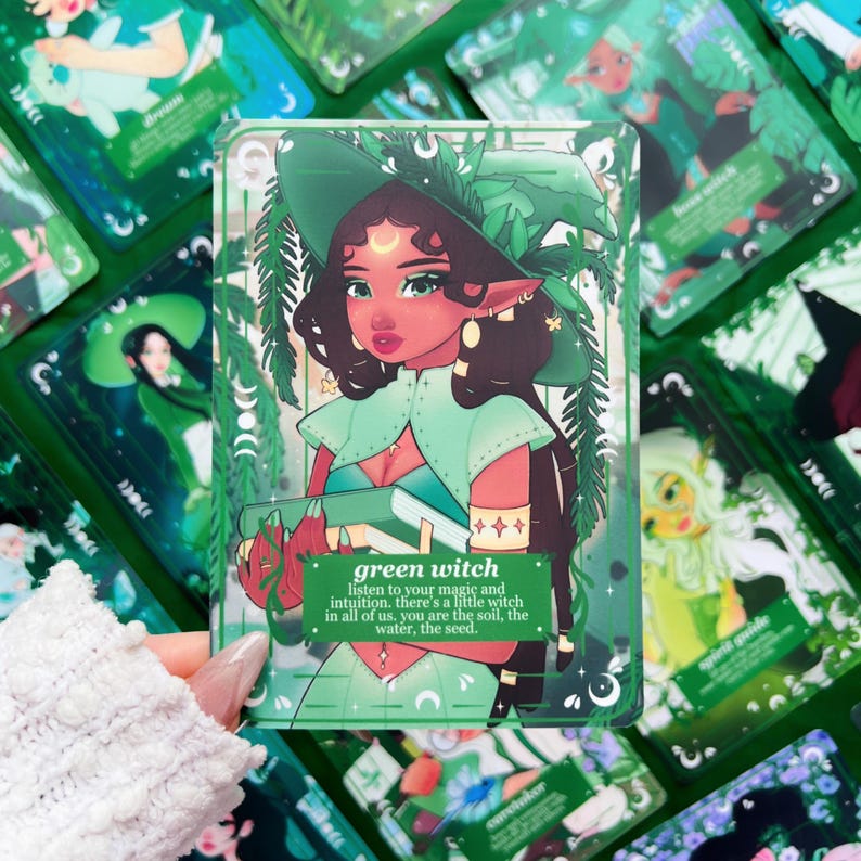 Peut inclure: Illustration d'une sorci&egrave;re verte sur une carte, repr&eacute;sentant une femme aux cheveux fonc&eacute;s, un chapeau vert et une cape. La carte contient le texte "green witch" et une citation sur l'intuition. D'autres cartes avec des illustrations similaires sont en arri&egrave;re-plan.