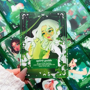 Peut inclure: Une carte de tarot verte et noire avec une illustration d'une femme aux longs cheveux blancs et d'un chat vert. La carte indique "spirit guide" avec du texte en dessous. D'autres cartes sont visibles en arri&egrave;re-plan.