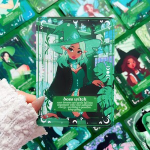 Peut inclure: Une carte de tarot verte et noire repr&eacute;sentant une sorci&egrave;re aux cheveux et au chapeau verts. La carte porte l'inscription "boss witch" et un message motivant. D'autres cartes similaires sont en arri&egrave;re-plan.