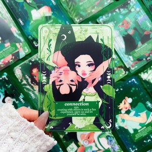 Peut inclure: Une carte de tarot verte avec une illustration de deux personnes s'embrassant, le mot "connection" et le num&eacute;ro "222". La carte est entour&eacute;e d'autres cartes de tarot avec des motifs verts et blancs. Le texte dit: cr&eacute;er avec les autres est une exp&eacute;rience si amusante. Ouvrez-vous et laissez-vous voir.