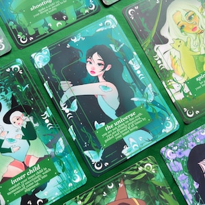 Puede incluir: Una colección de cartas de tarot con ilustraciones y texto. Las cartas presentan imágenes de mujeres, mariposas y elementos de la naturaleza en tonos verdes, azules y morados. El texto en las cartas incluye frases como "el universo" y "niño interior".