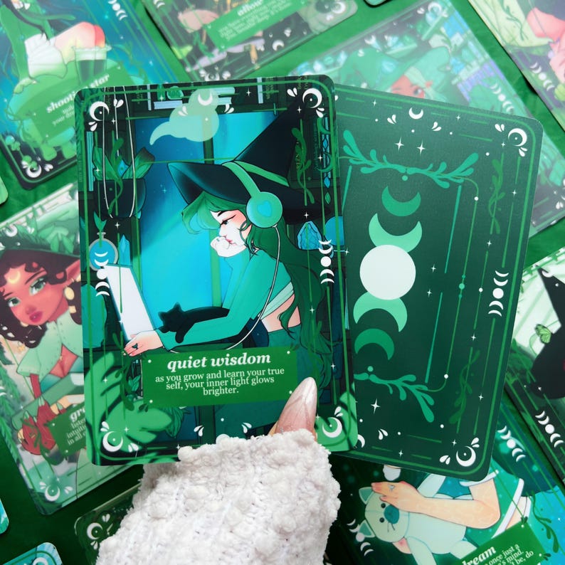Peut inclure: Carte de tarot verte avec une sorci&egrave;re portant un casque, un chat noir et le texte "quiet wisdom". Le dos de la carte pr&eacute;sente un motif de croissant de lune. D'autres cartes avec des illustrations similaires sont visibles.