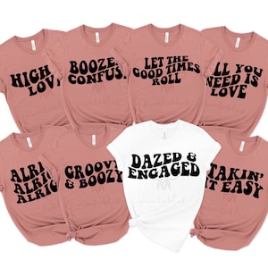 May include: Seven t-shirts with different retro-style text designs in black on a pink and white background. The text on the shirts includes "High Love", "Booze Confus", "Let the Good Times Roll", "All You Need is Love", "Alri Alri Alrig", "Groovy & Boozy", "Dazed & Engaged", and "Takin' It Easy".