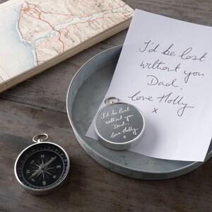 May include: A silver compass with a handwritten message on the face that reads "I'd be lost without you Dad, love Holly x". The compass is sitting on a silver tray with a white piece of paper with the same message written on it.