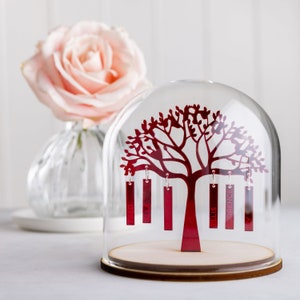 Könnte beinhalten: Eine rote Metallbaum-Silhouette mit Namen, die an den Ästen hängen, in einer durchsichtigen Glaskuppel. Die Namen sind "Fred", "Ella", "Penny", "Ellis" und "Opence".