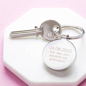 May include: Silver keychain with a round charm engraved with the date 04.08.2015 and the text "the day you became my godmother".