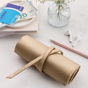 May include: A gold leather pencil case with a strap closure. The case is rolled up and tied with the strap.