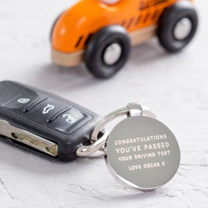 May include: Silver keychain with a round tag that reads "Congratulations you've passed your driving test Love Oscar X".