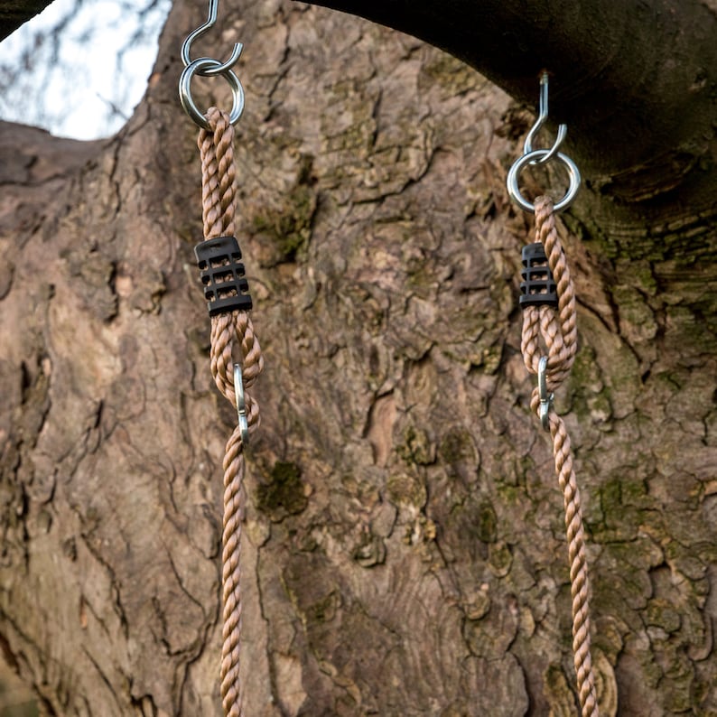 May include: Two brown rope swings hanging from a tree branch. Each swing has a silver hook and a black plastic connector.