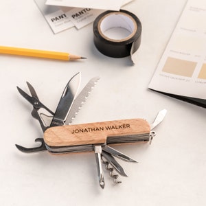 Op de afbeelding: Een multifunctioneel zakmes met een houten handvat gegraveerd met de naam "JONATHAN WALKER". Het mes heeft een verscheidenheid aan gereedschappen, waaronder een mes, een zaag, een flesopener, een schroevendraaier en een kurkentrekker.