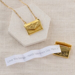 May include: A gold necklace with a small, ornate envelope pendant. The envelope opens to reveal a small piece of paper with the message "Love You Georgia - Happy Valentine's Day, Mark x".