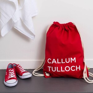 Op de afbeelding: Rode trekkoordtas met witte tekst die "CALLUM TULLOCH" luidt.