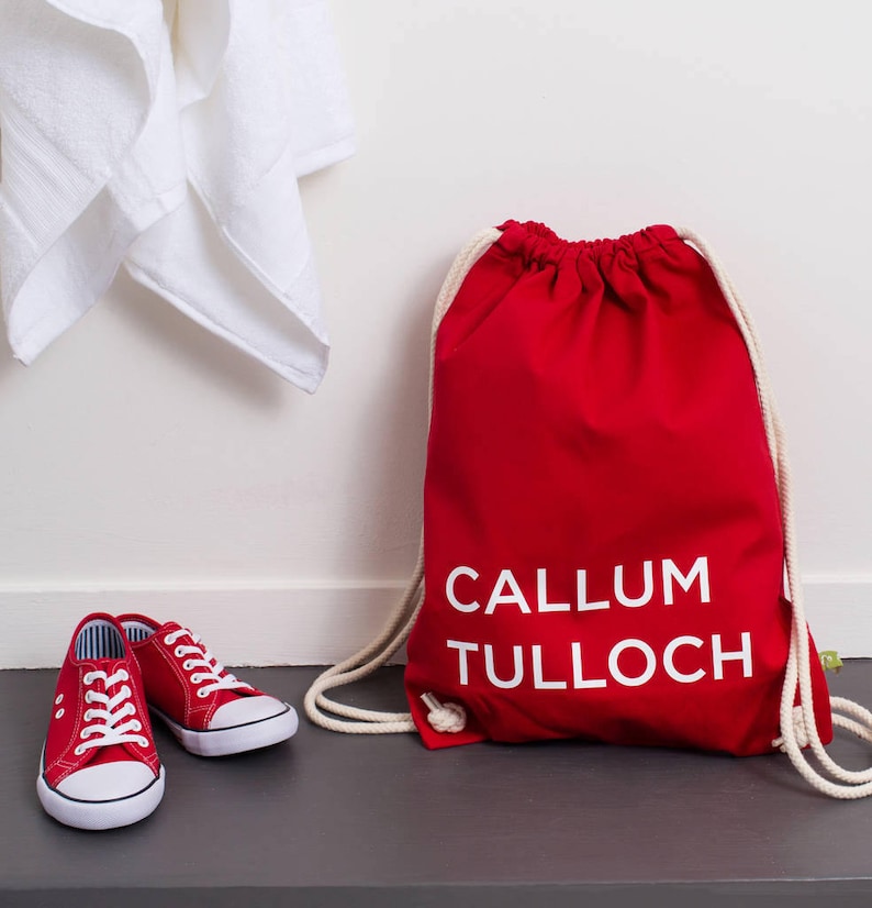 Op de afbeelding: Rode trekkoordtas met witte tekst die "CALLUM TULLOCH" luidt.