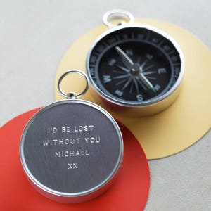 Op de afbeelding: Twee zilveren zakkompassen. Een kompas heeft een zwart gezicht met een kompasnaald en het andere kompas heeft een zilveren gezicht met de inscriptie "I'd be lost without you Michael XX".