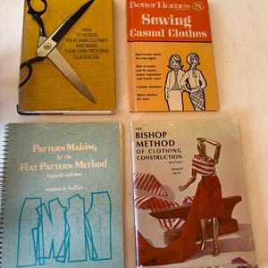 Può includere: Quattro libri vintage di cucito e modellistica. Un libro giallo con delle forbici, un libro arancione intitolato Better Homes Sewing Casual Clothes, un libro blu a spirale intitolato Pattern Making e un libro intitolato The Bishop Method.