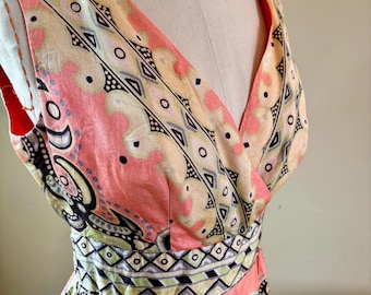 May include: A sleeveless, V-neck dress with a colorful paisley pattern. The dress features a pink background with geometric and floral designs in black, white, yellow, and green. The waistline is accentuated with a patterned band.
