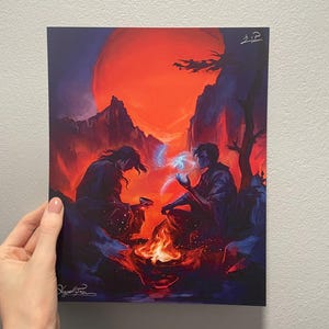 May include: A print depicting two figures seated near a campfire under a large red sun. The artwork features a dramatic color palette of reds, blues, and purples, with the figures seemingly interacting with glowing orbs. The print is held by a hand.