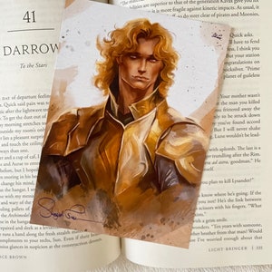 May include: A close-up of a book cover with a young man with blond hair and blue eyes. The book cover is a light brown color with a dark brown border. The text on the cover reads "Darrow To the Stars".
