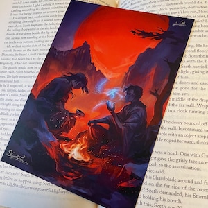 May include: Two figures, one with dark hair and one with light hair, sit facing each other by a campfire. They are both wearing dark clothing. The background is a dark, rocky landscape with a large red moon in the sky.