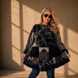 Op de afbeelding: Een tuniek met lange mouwen in een patchworkontwerp met zwarte en grijze stoffen panelen. Het kledingstuk bevat een zwart-witte marmerprint, een gewatteerd gedeelte, een spijkerzak met zilveren studs en een donkere spijkerstof zoom onderaan.