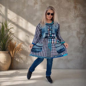 Op de afbeelding: Een tuniek met lange mouwen met een patchworkontwerp van geruite stof, denimpanelen en stippenaccenten. Het kledingstuk is voorzien van een vetersluiting aan de voorzijde, twee grote denim zakken en een uitlopende zoom, gecombineerd met een blauwe spijkerbroek.
