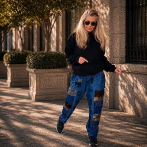 May include: A black long-sleeved sweatshirt paired with blue denim pants featuring various rectangular patchwork panels in different shades of blue, dark brown, and gold, finished with black athletic sneakers and dark-tinted sunglasses.