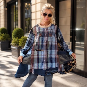 Peut inclure: Une chemise à manches longues boutonnée présentant un design en patchwork composé de tissu à carreaux bleu et marron, de panneaux en jean foncé et de tissu noir à motifs floraux dorés. Elle possède un col beige rond, deux poches poitrine.