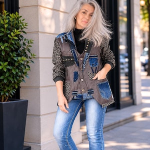 May include: A patchwork blazer featuring denim, leopard print, and pinstripe elements. The jacket showcases a distinctive design with various textures and colours, including blue, brown, and black. The model is wearing blue jeans and a black turtleneck.