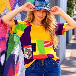 Peut inclure: Un t-shirt à manches courtes en patchwork composé de blocs vibrants jaunes, violets, verts et rouges, avec une poche ornée d'un imprimé floral, d'un motif à carreaux noir et blanc et de rayures rouges, porté avec une casquette en jean bleu usé.