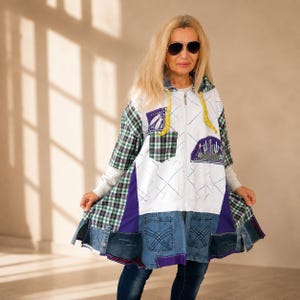 May include: A patchwork jacket with a white base, featuring a plaid pattern, denim accents, and purple details. The jacket has a hood with a yellow drawstring and a zipper closure. Patches include a desert scene and a feather design.