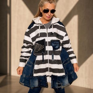 Puede incluir: Una chaqueta con capucha y cremallera que presenta un patrón de rayas horizontales en blanco y negro. La prenda está adornada con varios parches de mezclilla azul oscuro, incluyendo una sección con tachuelas metálicas y bordes deshilachados.