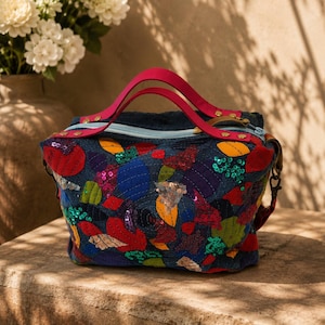 May include: A dark blue denim handbag featuring vibrant, multi-coloured fabric patches in red, yellow, green, and blue. The bag is adorned with sparkling sequins and has two bright pink top handles, a light blue zip, and gold-tone metal hardware.