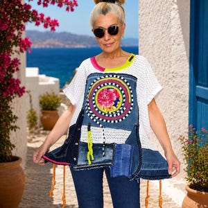 Könnte beinhalten: Ein weißes Kurzarm-Oberteil aus Netzstoff mit einem Patchwork-Design aus dunkelblauen Denim-Einsätzen, einem zentralen kreisförmigen Blumenmuster, neongelben Akzenten und orangefarbenen hängenden Schnüren am Saum, kombiniert mit einer blauen Jeans.