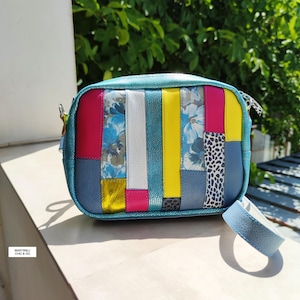 以下が含まれることがあります： パッチワークデザインのカラフルなクロスボディバッグ。青、ピンク、黄色、白、花柄など、さまざまな色を使用しています。青いストラップとジッパー開閉部があります。「MARTINELLI CHIC & GO」の文字が見えます。